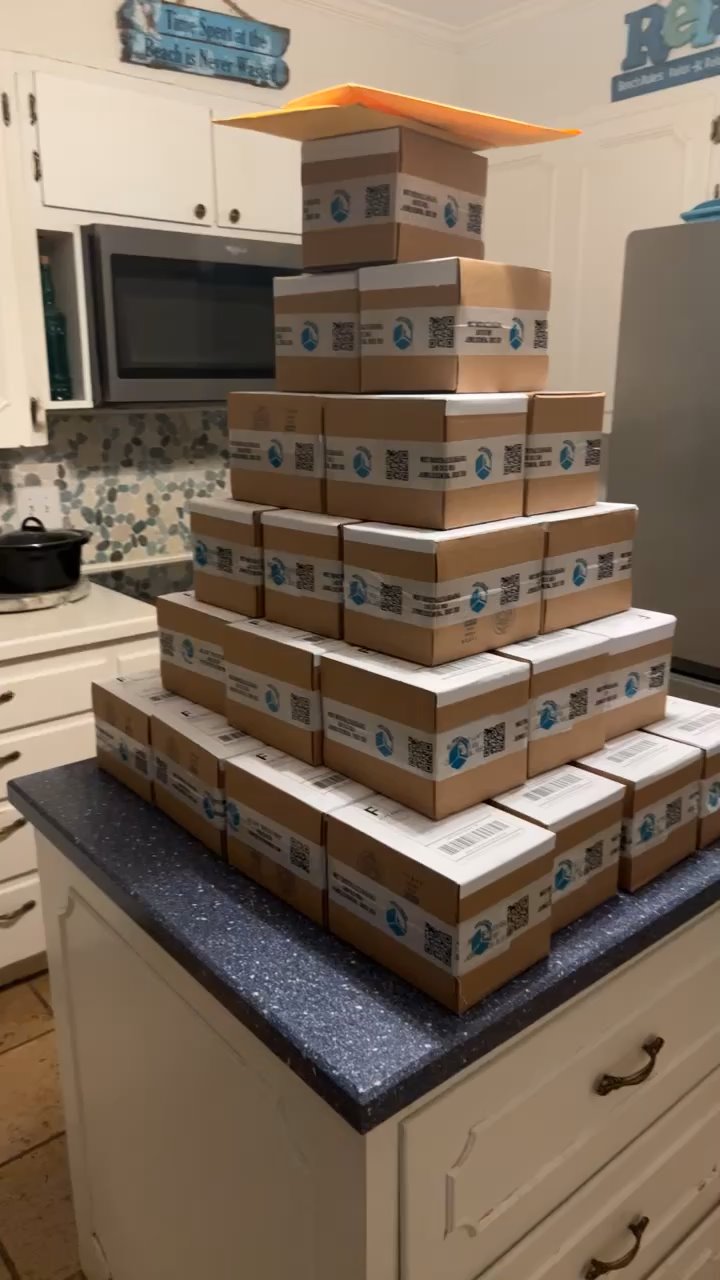 Stacked pyramid of branded Perfect Packing boxes on a kitchen island, each labeled with logo and QR code, showcasing order volume and shipping readiness.